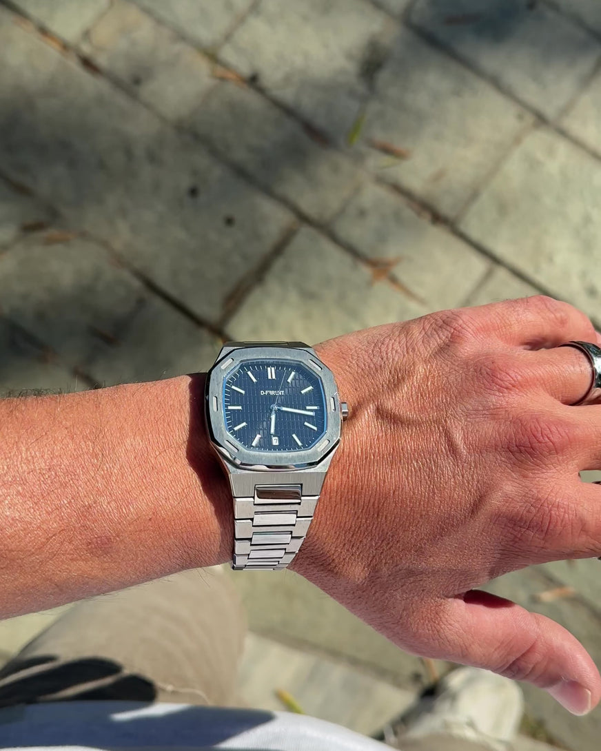 D-FFRENT The Aura Black stainless steel men's watch on wrist in sunlight with integrated bracelet and black textured dial.